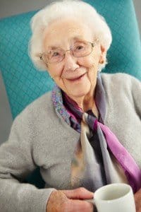 A elderly woman sitting in a chair with a coffee cup in her hand smiling