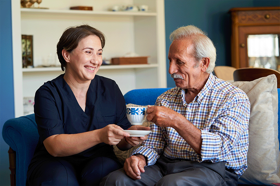 A middle age woman and elderly man sitting on the couch sharing tea.