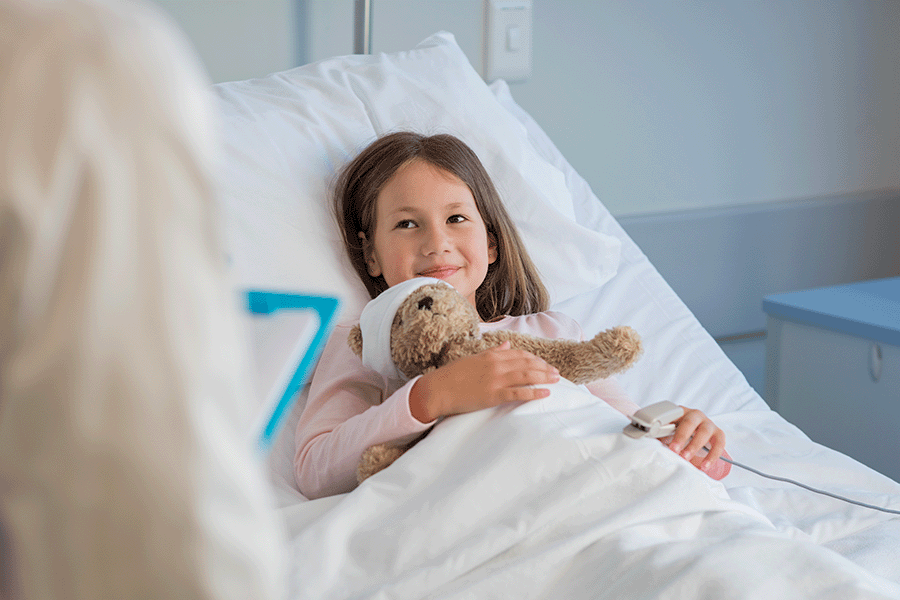 A little girl laying in the hospital bed with a teddy bear in her arm.